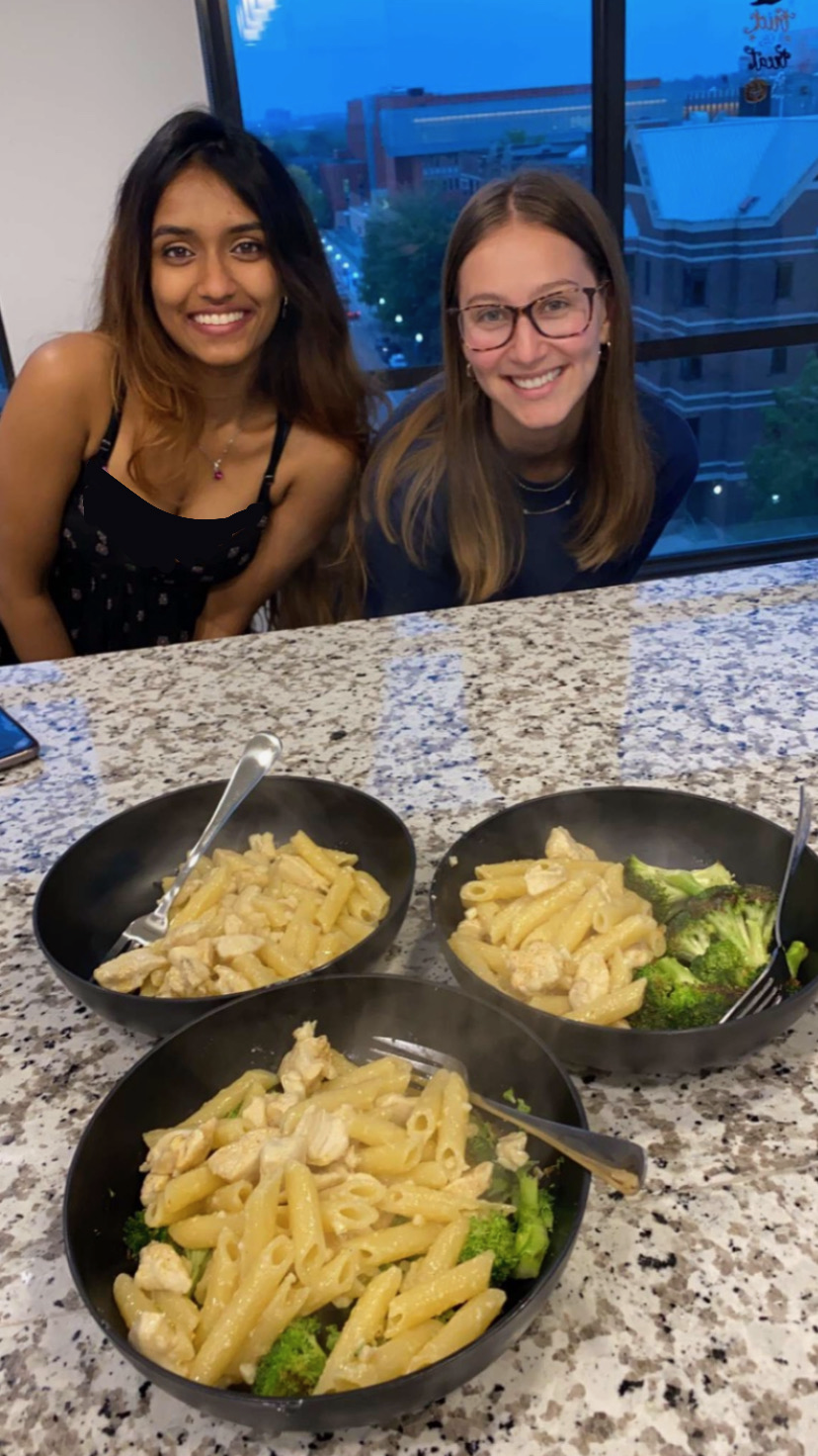 Two girls are smiling at the camera. There are three bowls of pasta in front of them.