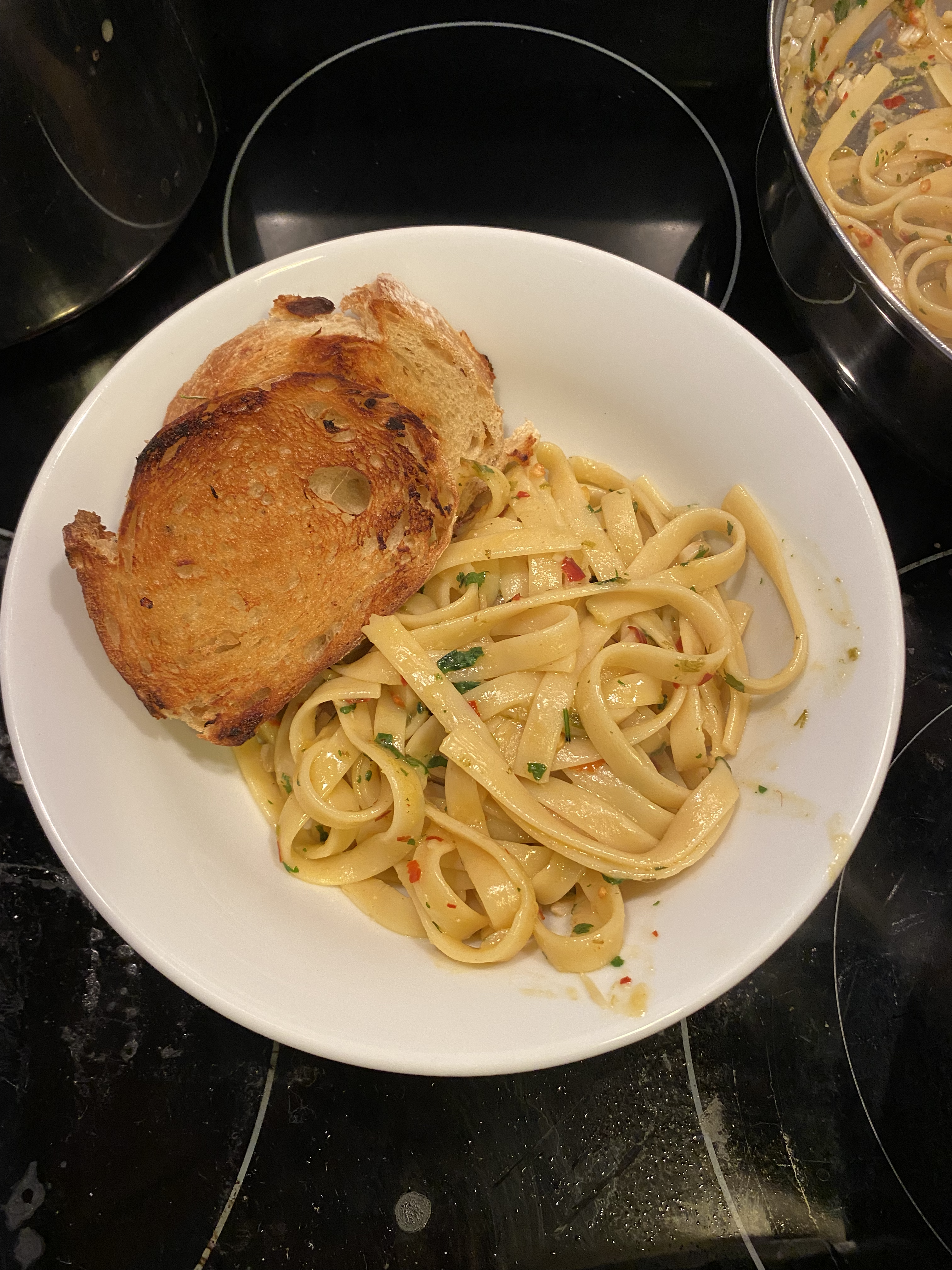 A bowl of lemon garlic pasta garnished with red pepper flakes and parsley. There is a side of toasted garlic bread.